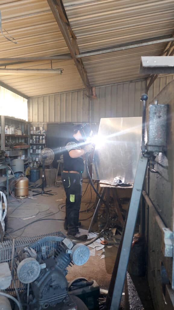 Artisan soudeur avec casque travaillant une plaque de métal en atelier, éclat lumineux de soudure à l'arc.
